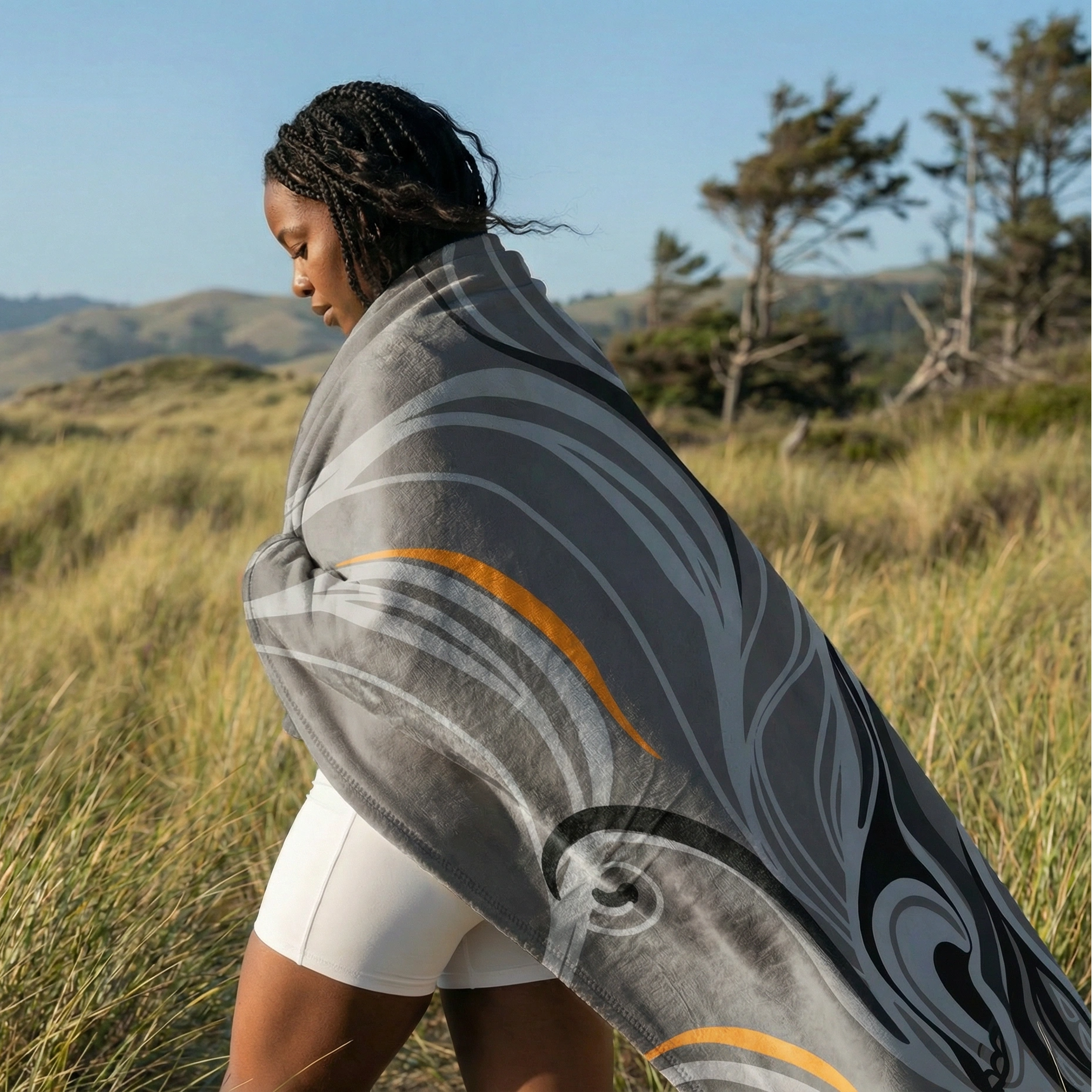 Person wrapped in a gray and orange abstract art fleece blanket while walking outdoors in a grassy landscape, highlighting warmth, comfort, and modern artistic design