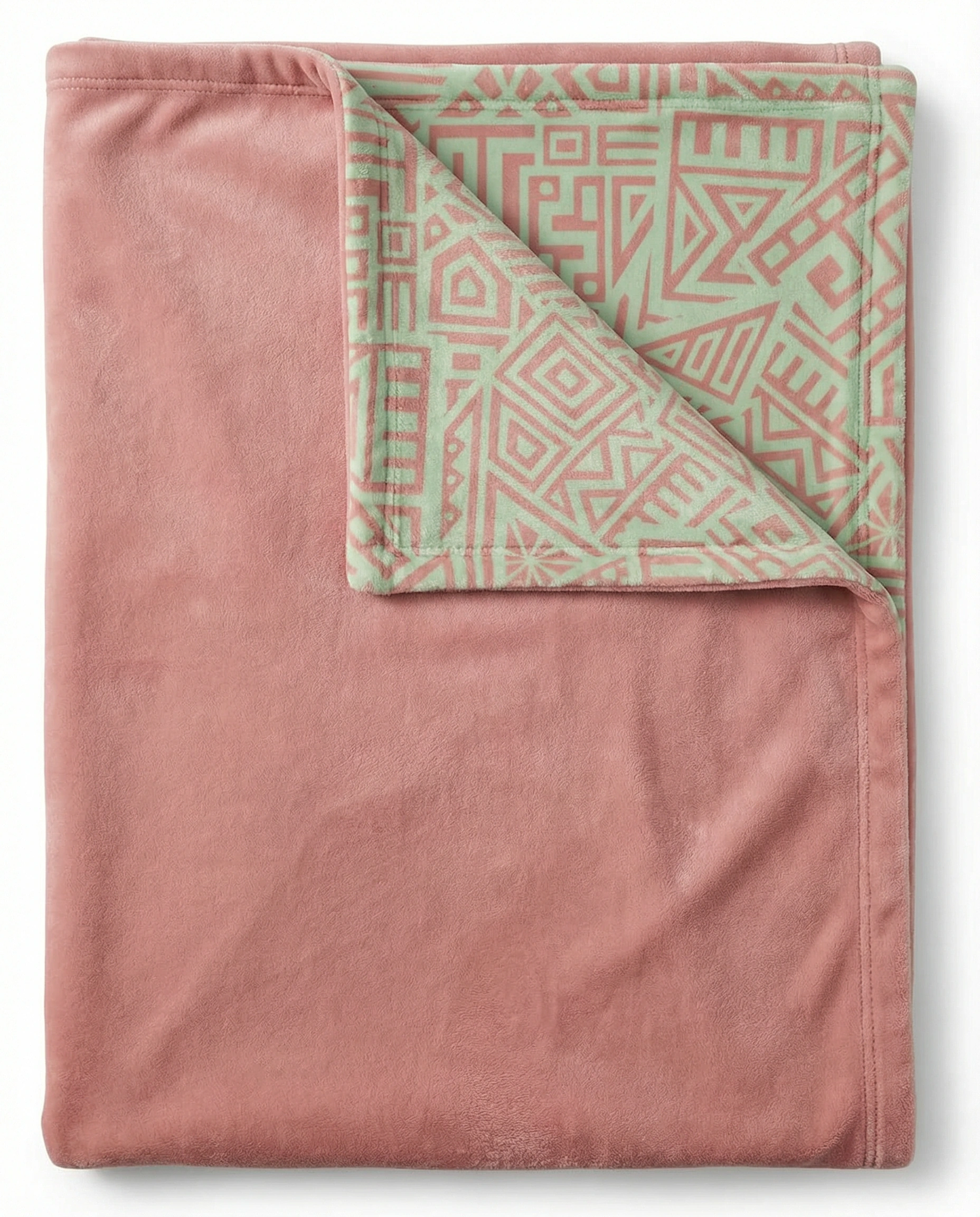 Folded reversible pink fleece blanket displaying a solid blush side and an African geometric pattern lining, highlighting its soft plush texture