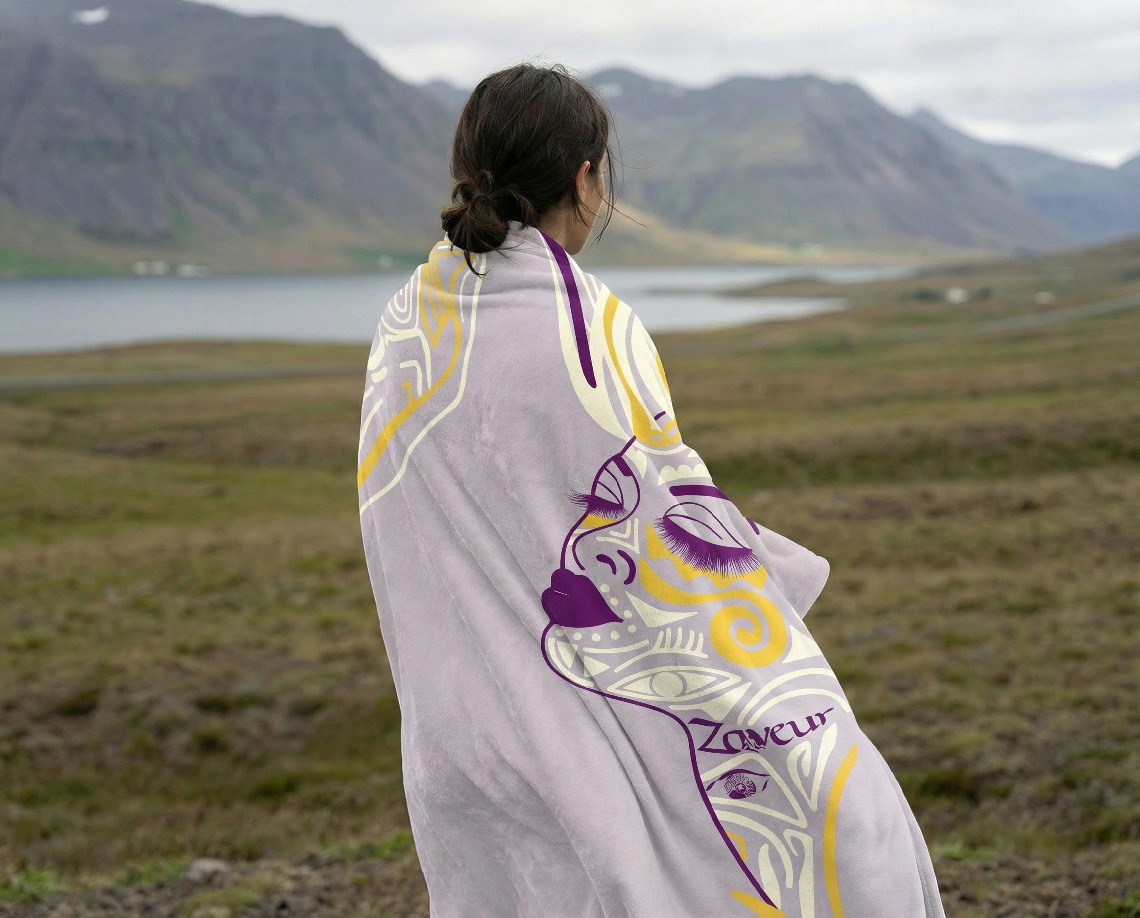 Person wearing a reversible purple and yellow abstract art fleece blanket in an open landscape, highlighting warmth, comfort, and artistic design.