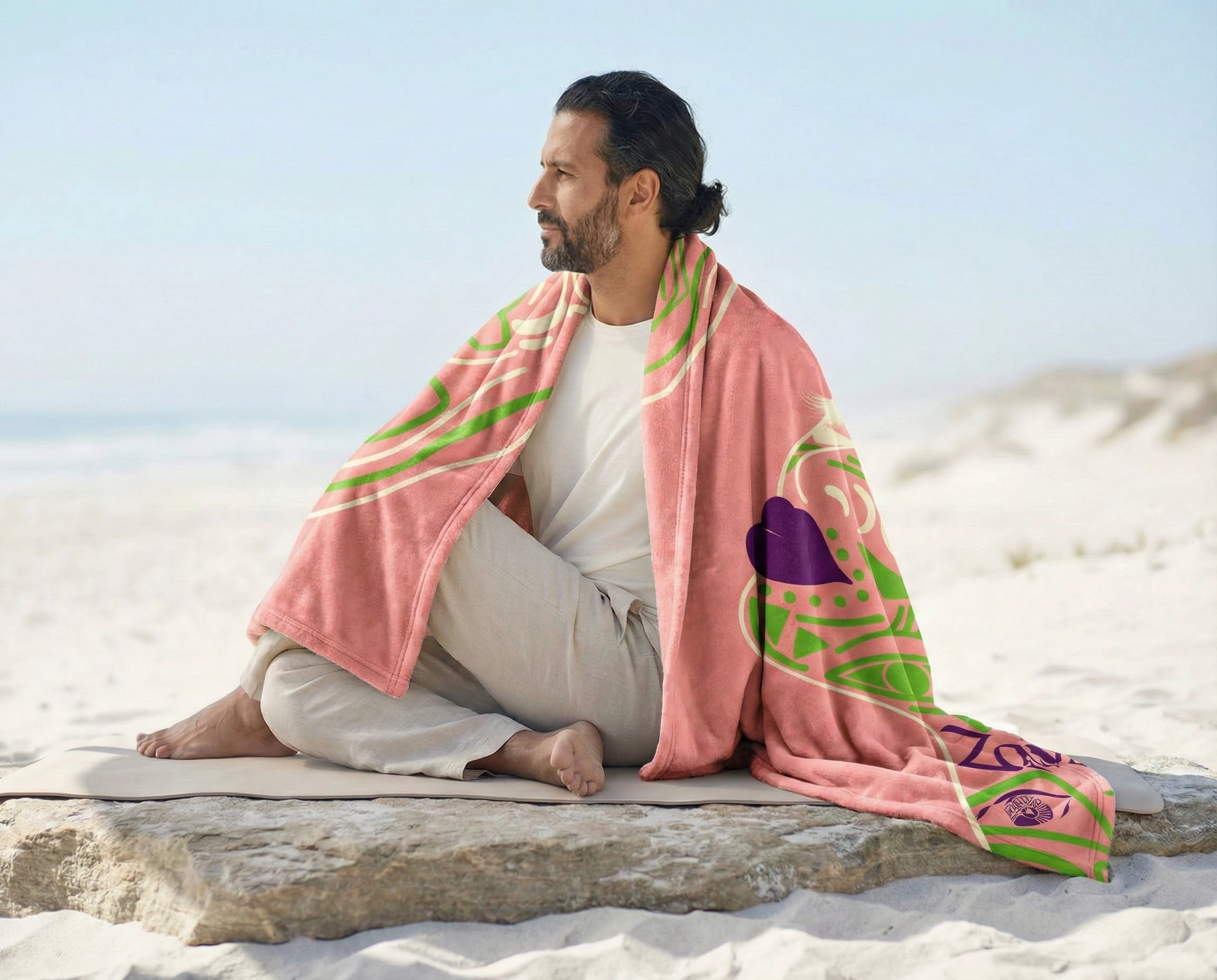 Man sitting outdoors wrapped in a pink and green abstract art throw blanket in a calm minimalist setting