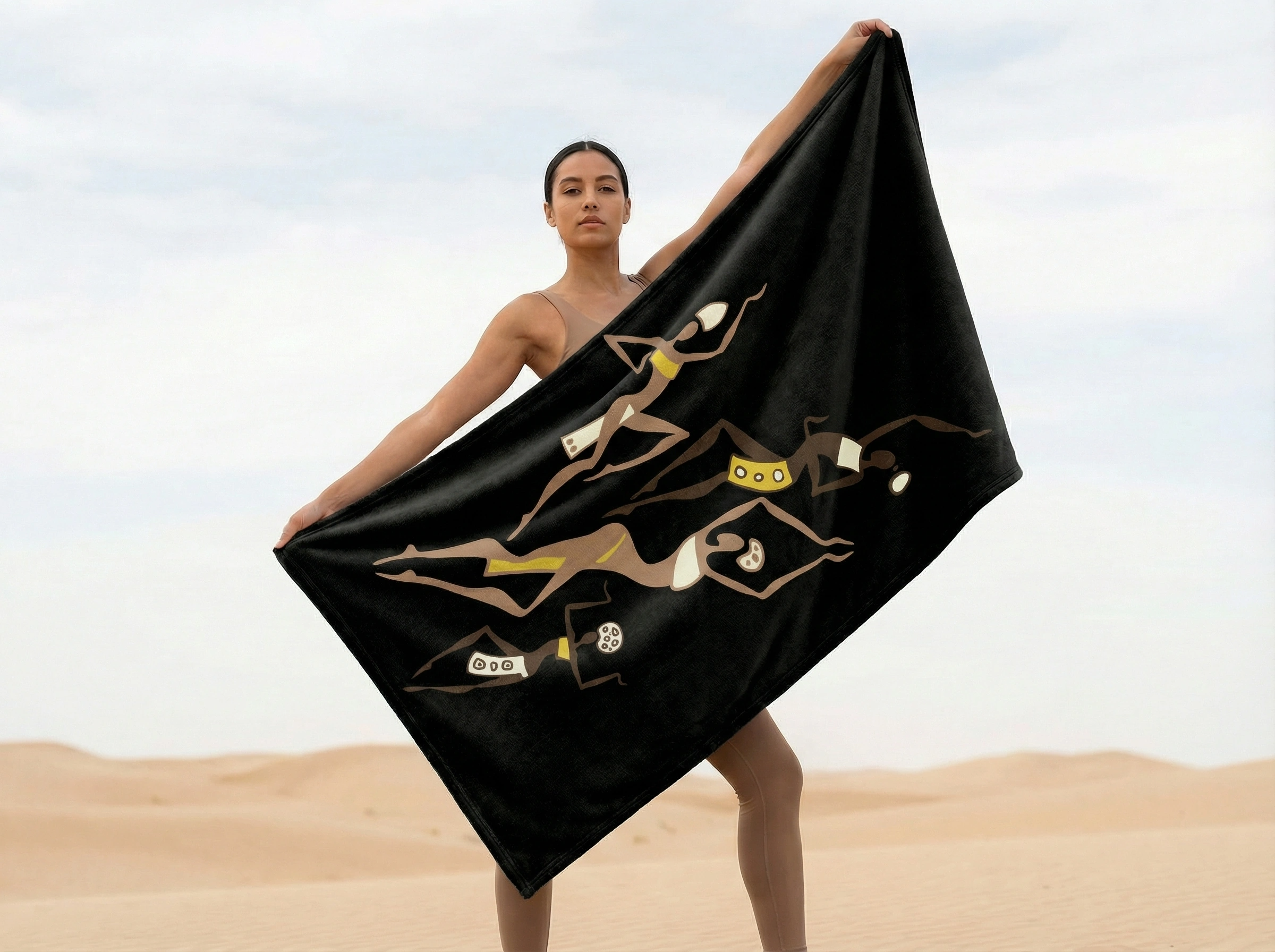 Person holding a black fleece blanket featuring African tribal dancer artwork in a desert landscape, showcasing bold cultural design, movement, and artistic expression