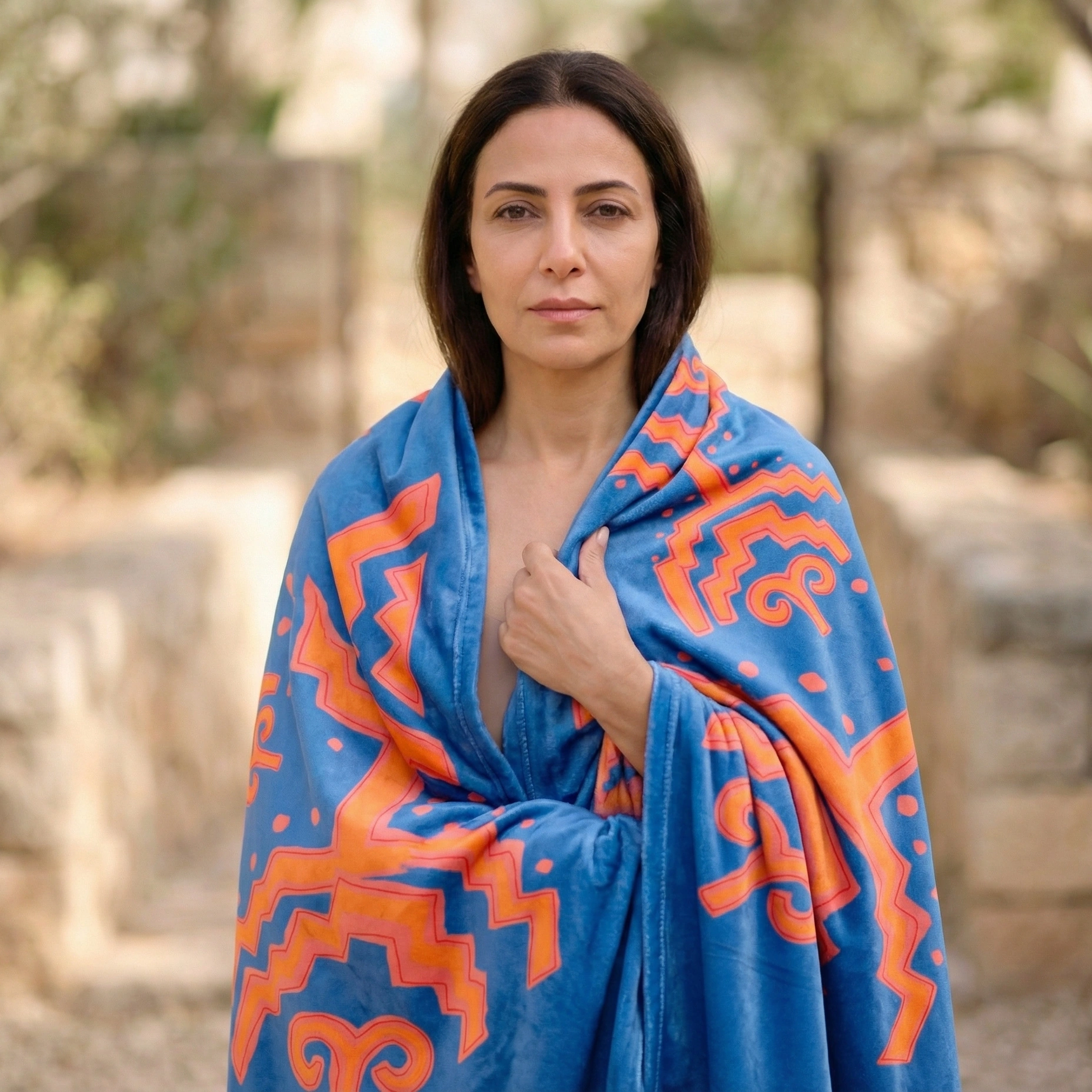 Person wearing a blue meditation blanket with bold geometric patterns, wrapped around the shoulders in a natural outdoor setting.