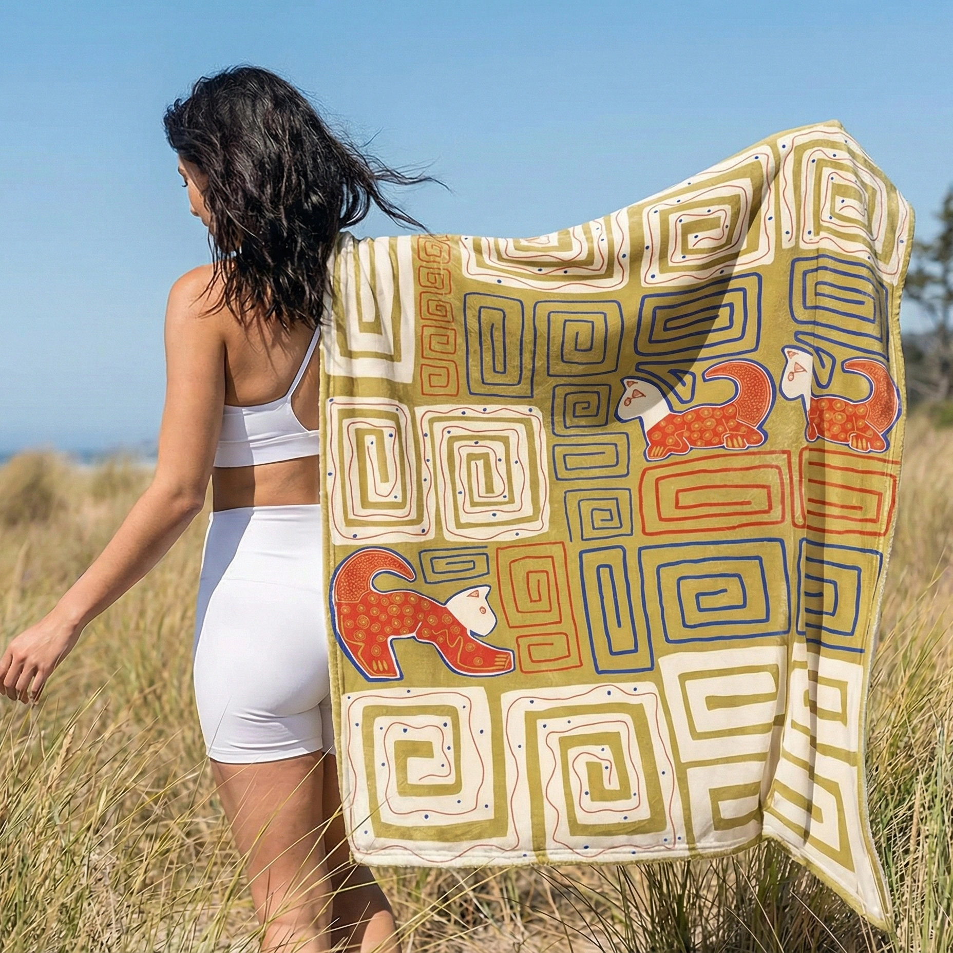 Person holding a gold-colored meditation blanket with soft geometric textures near a lake in a peaceful outdoor environment.
